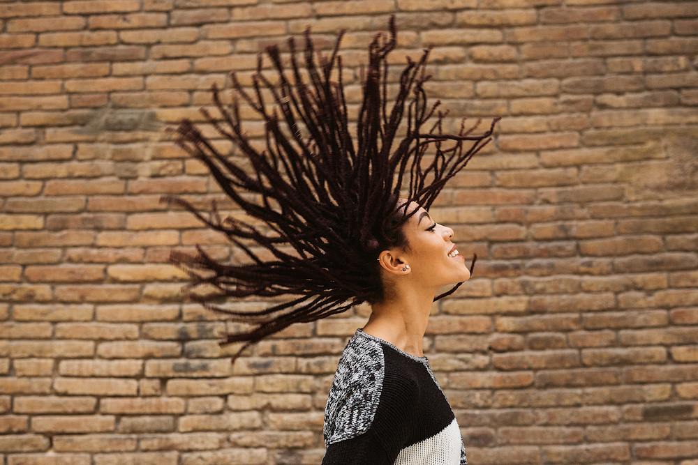 Black woman with flying locs standing against brick wall